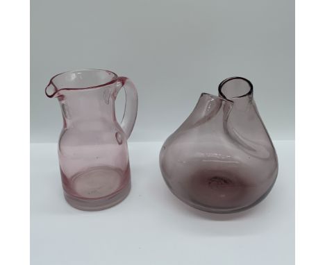 A charming set of two hand-blown pink glass items, featuring a pitcher and a vase. The pitcher showcases a delicate curved ha