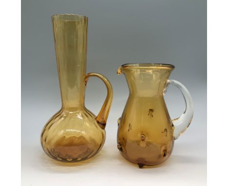This set features two elegant handblown amber glass pitchers, both showcasing distinctive shapes and textures. One pitcher ha