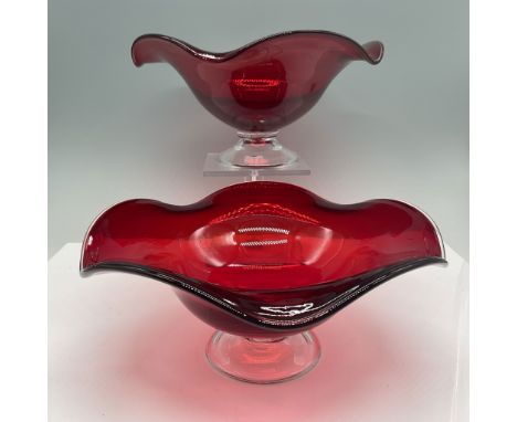 Pair of elegant ruby red glass bowls featuring flared, ruffled edges and clear pedestal bases. The vibrant ruby hue highlight