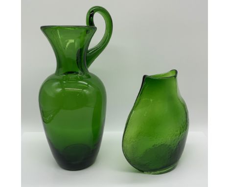 A striking pair of hand-blown green glass vessels featuring unique shapes and vibrant coloring. The first piece is a pitcher-