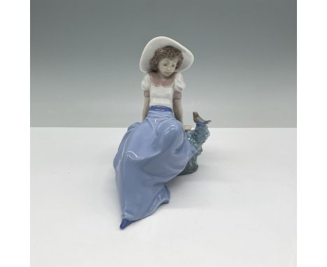 Charming porcelain figurine by Nao, a division of Lladro, depicting a young girl seated gracefully on a rock with a delicate 
