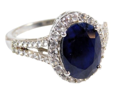 A sapphire and CZ ring, the oval cut sapphire in a surround of brilliant CZs, in a basket mount, white metal, stamped 925, si