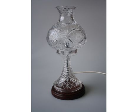 A 20TH CENTURY CUT-GLASS TABLE LAMP, with globular detachable shade and tapering stem, raised on a wooden plinth base. 42.5cm