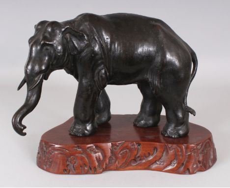 A SIGNED JAPANESE MEIJI PERIOD BRONZE MODEL OF A STANDING ELEPHANT, together with a wood stand, the underside of the elephant