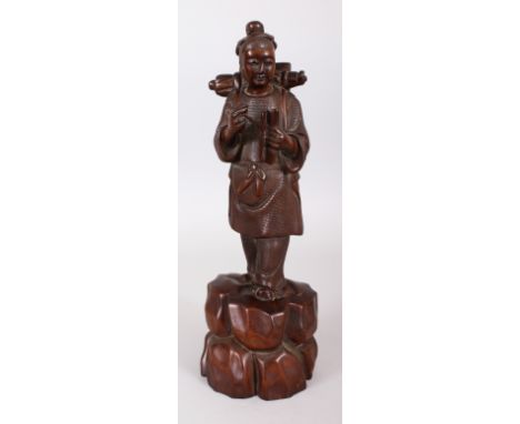 A 20TH CENTURY CHINESE CARVED WOOD FIGURE OF A YOUTH STANDING ON A ROCKY PLINTH, holding in his hands a scroll and a pen, 12.