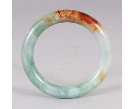 A CHINESE CELADON JADE BANGLE, the stone with an area of russet inclusions, 3.25in diameter, the inner rim 2.25in diameter.
