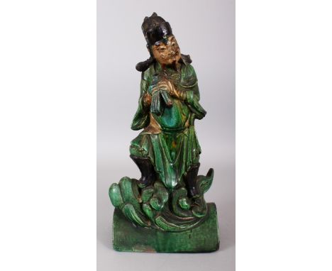 A GOOD CHINESE MING DYNASTY GREEN GLAZED POTTERY ROOF TILE OF A CLOUD BORNE IMMORTAL, clasping two tablets, 7.1in wide &amp; 