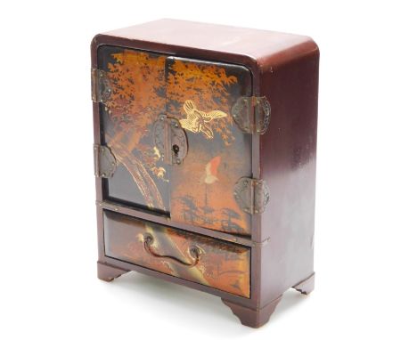 A Japanese Taisho period lacquered table cabinet, repousse decorated with birds in flight before trees, with elaborate escutc