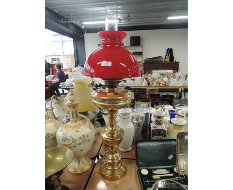 A tall standing brass bodied oil burning lamp with red shade