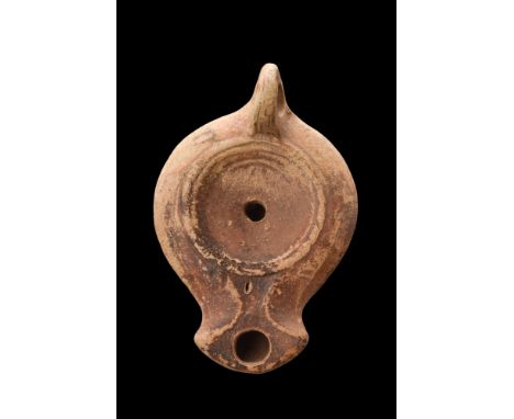 Ca. 100-200 AD. A terracotta oil lamp with a sunken discus with a centrally located filling hole. The tondo is circled by a s