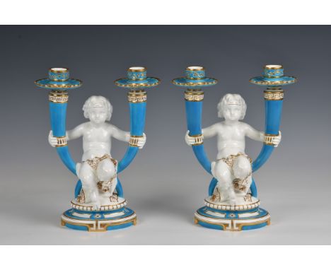 A pair of Minton twin branch candelabras of a central Cherub holding on each hand an outswept candlestick, seated on an oval 