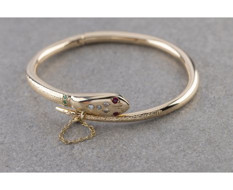 A 9ct yellow gold snake bangle,  rubies for eyes, diamonds to head and emeralds to collar, hinged with pin fastener, internal