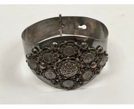 A white metal bangle with pictorial rounders and foliate scrolled decoration 