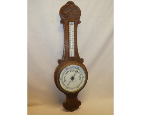 A good quality aneroid barometer with circular ceramic dial below thermometer in carved oak case