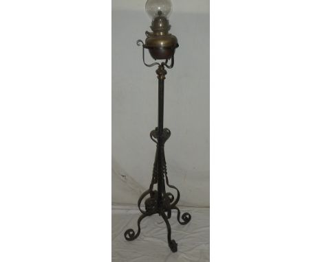 A wrought iron adjustable oil lamp standard supporting a brass oil lamp with glass chimney