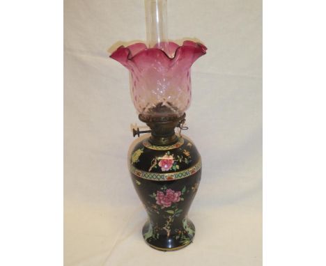 An Edwardian pottery tapered oil lamp with separate reservoir and brass mounts supporting a cranberry tinted glass shade (af)