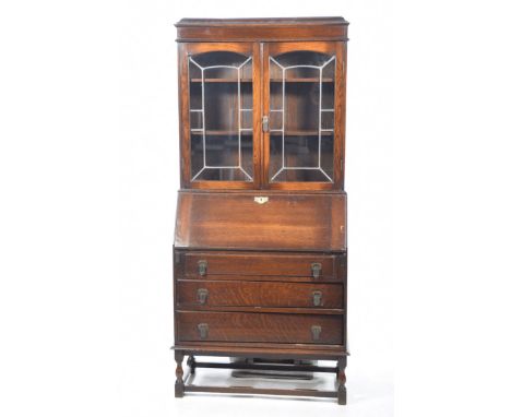 A 1930's oak bureau bookcase
With a caddy top above a plain frieze two glazed and leaded doors enclosing a pair of shelves ab