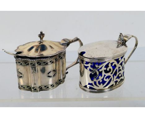 Two silver mustard pots with blue glass liners, the first of oval section with pierced scrolling decoration, Birmingham assay