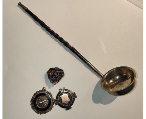 A silver and gold medal, another silver badge, a swimming medal and a white metal and turned handled ladle. 