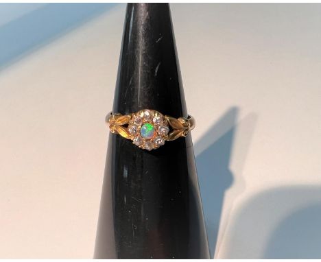An 18 carat hallmarked gold ring with opal and diamonds in flower head cluster setting, with twin leaf motifs to the shoulder