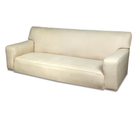 Betty Joel, a large cream upholstered modernist sofa, with squared arms and raised on casters 84 x 230 x 90cm (33 x 90 x 35in