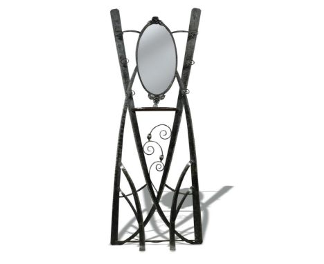 Attributed to Goberg, a wrought iron hall stand, the hammered strap work frame with oval mirror plate and shelf above a scrol