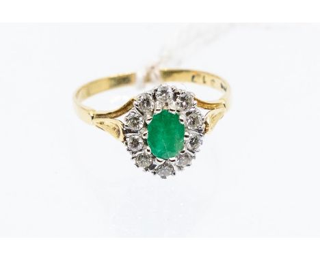 An emerald and diamond 18ct gold cluster ring, comprising an oval claw set emerald to the centre, within a border of small di