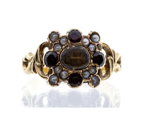 A Victorian mourning ring, the centre with hair compartment, within a border of flat cut round garnets and seed pearls, folia