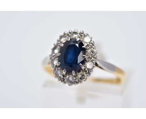 A YELLOW METAL SAPPHIRE AND DIAMOND CLUSTER RING, designed with an oval cut claw set blue sapphire within a round brilliant c