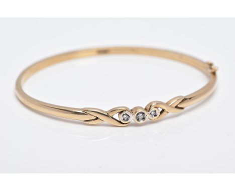 A 9CT GOLD DIAMOND BANGLE, designed with a crossover section set with three round brilliant cut diamonds each within a collet