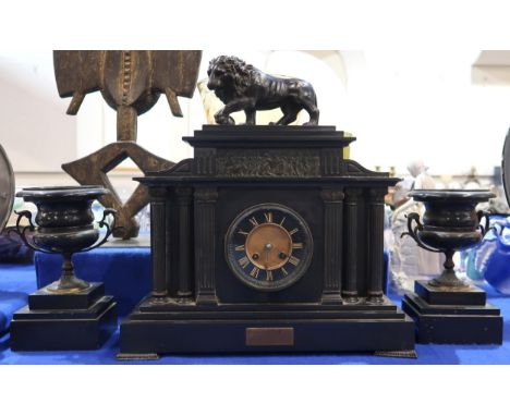 A slate mantle clock with spelter Medici lion finial with a pair of urn shaped garnitures Condition Report:Available upon req