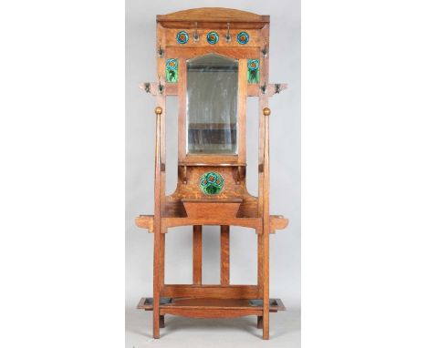 An Edwardian Arts and Crafts Glasgow School oak hallstand, the mirrored back inset with glazed ceramic tiles, the front uprig