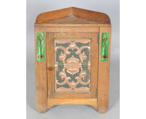 An Edwardian Arts and Crafts oak hanging corner cabinet, possibly by Liberty &amp; Co, the door inset with a copper panel fla