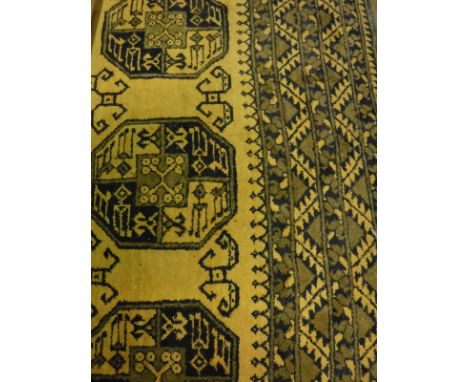 A Bokhara rug, the central panel set with repeating medallions on a mustard / gold ground, within a stepped brown and gold bo