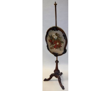 A Victorian walnut framed pole screen with needlework upholstered panel raised on a tripod base 