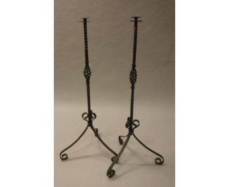 A pair of 20th century wrought iron floor standing candle holders on scrolling tripod supports