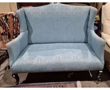 Edwardian wingback two-seat sofa in pale blue upholstery, with cabriole front legs to castors 