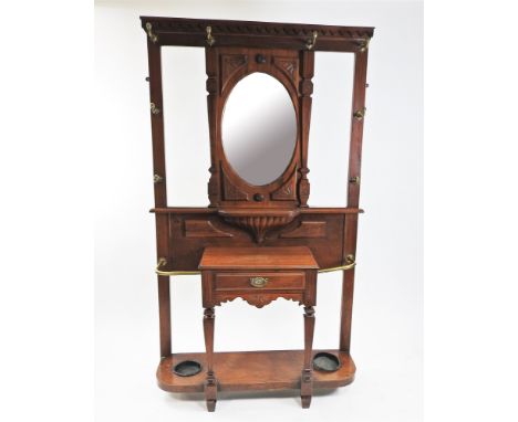 A late Victorian walnut hall stand with tooth moulded top rail above an oval bevelled mirror and with eight brass coat hooks 