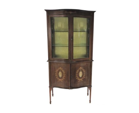 An Edwardian mahogany and inlaid serpentine front display cabinet in Adam revival style, the two glazed doors enclosing two g