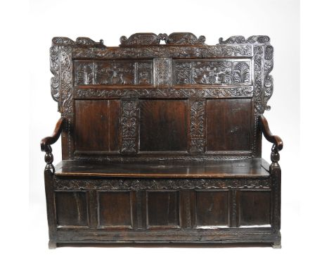 A joined oak box seat settle, early 18th century and later, the ornate five panel back surmounted by a winged head bracket, f