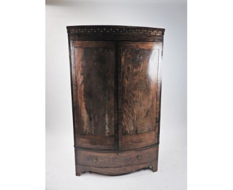A mahogany bow front wardrobe, 19 th century, with acorn moulded cornice above two crossbanded panel doors enclosing a hangin