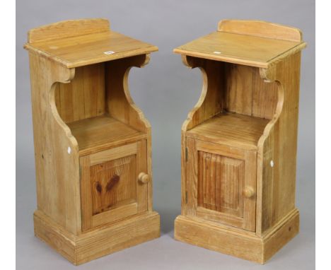 A pair of pine bedside cabinets each with an open recess above cupboard enclosed by a fielded panel door, &amp; on a plinth b