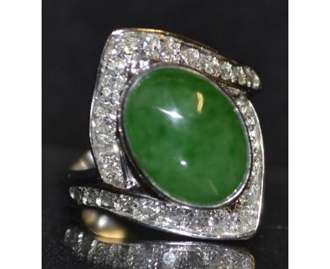 A jade and diamond ring, central oval green jade cabochon, open crest encrusted with twenty eight round cut diamonds, 14ct wh
