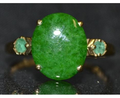 A deep green jade and emerald trilogy ring, central oval jade cabochon, flanked to each side by a single round emerald, 9ct g