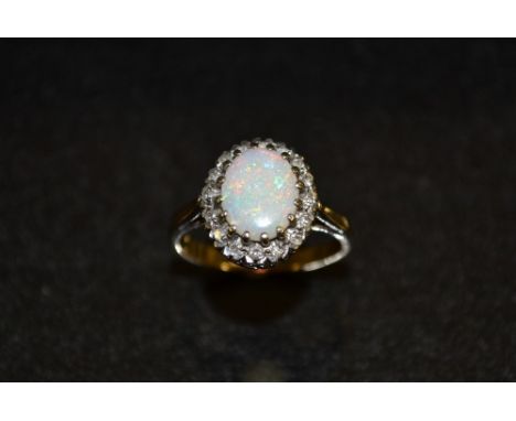 An opal and diamond ring, central oval opal, flashing red, green, blue and violet colour play, above a band of sixteen round 