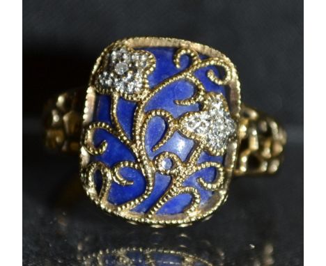 A diamond and lapis lazuli dress ring, scrolling floral basket inset with two diamond accented flower heads, above a rounded 