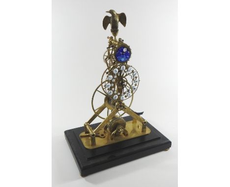 A brass skeleton clock, surmounted by an eagle, with enamel moon phase above enamel hours showing Roman numerals, housed in a