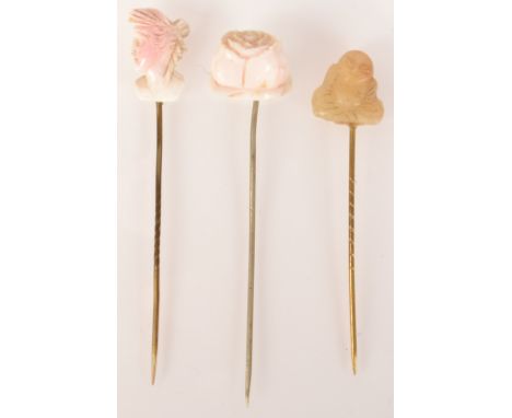 A jade Buddha pin and two carved pale pink pins.