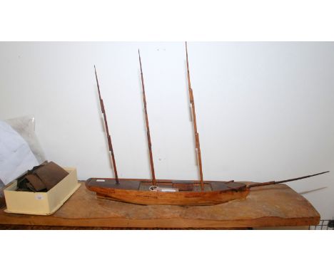 A scale model of a schooner in mid restoration, the solid hull sits in a carved wood ocean, shaped wooden sails. length of hu