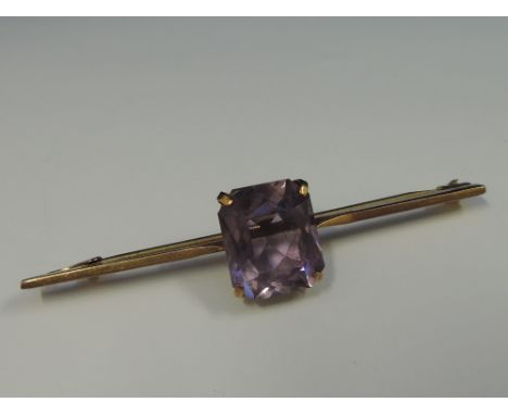 A yellow metal bar brooch stamped 9ct set with a amethyst style square stone 